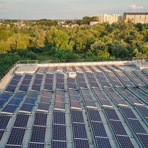 Rooftop solar panels installed on an industrial building, surrounded by trees and suburban landscape in the background.