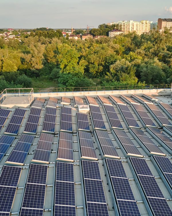 Rooftop solar panels installed on an industrial building, surrounded by trees and suburban landscape in the background.