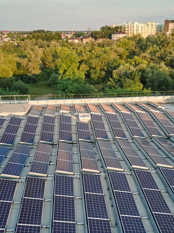 Rooftop solar panels installed on an industrial building, surrounded by trees and suburban landscape in the background.