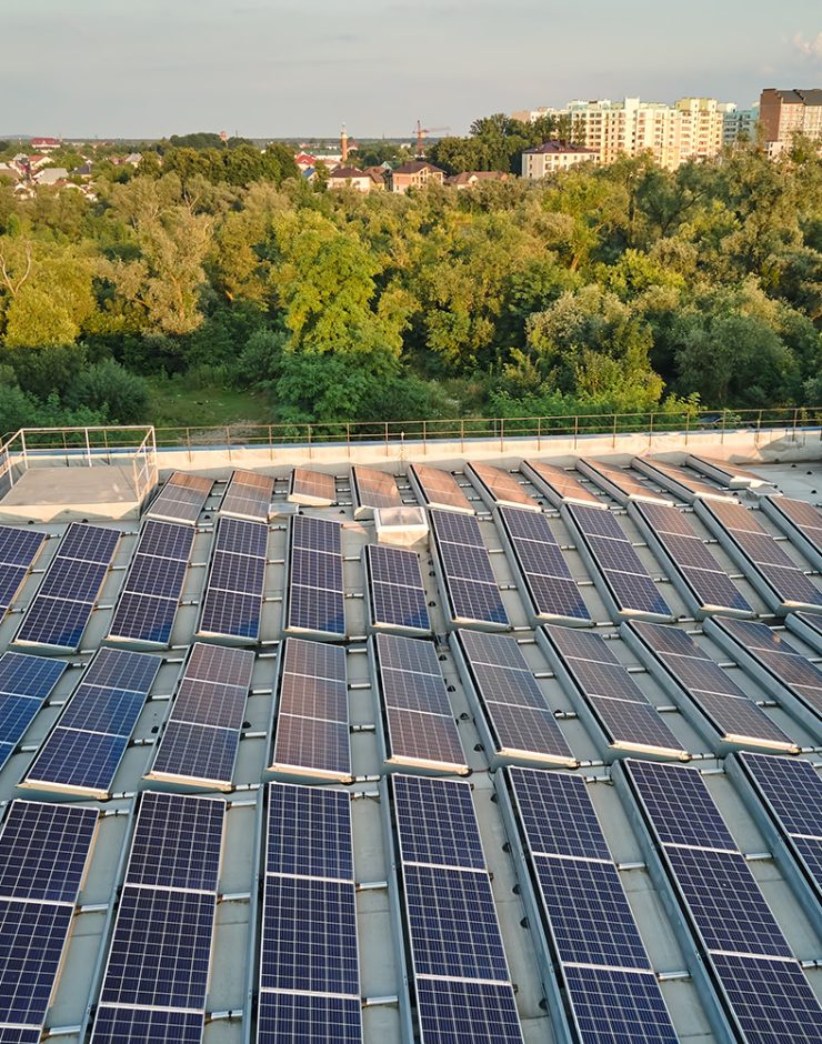 Rooftop solar panels installed on an industrial building, surrounded by trees and suburban landscape in the background.