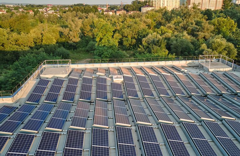 Rooftop solar panels installed on an industrial building, surrounded by trees and suburban landscape in the background.