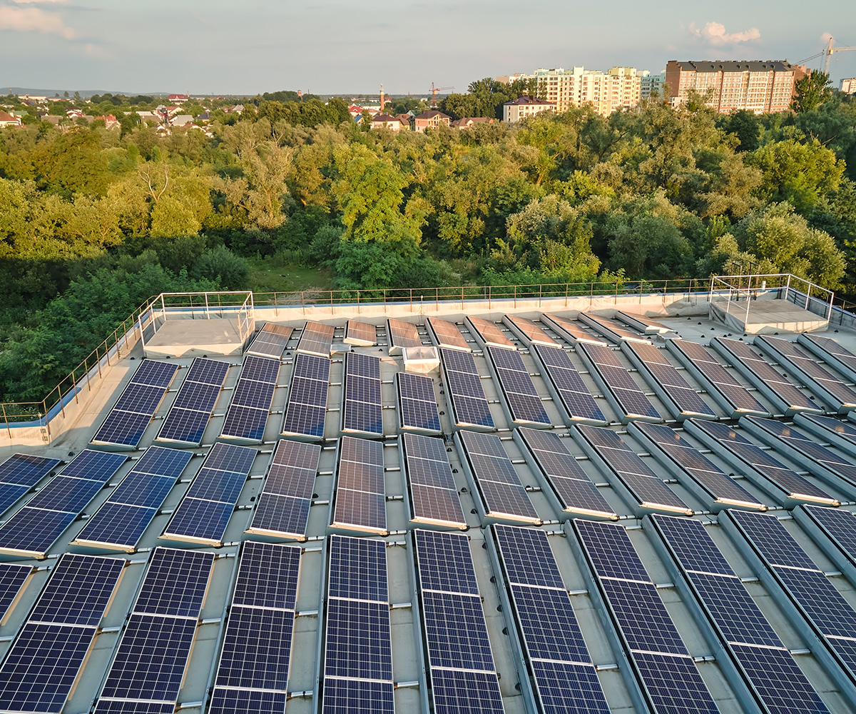 Rooftop solar panels installed on an industrial building, surrounded by trees and suburban landscape in the background.