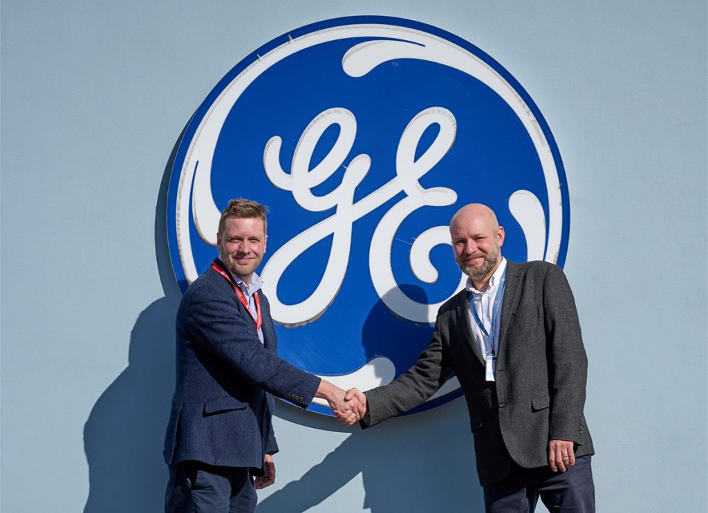 Ortus Energy's Alistair Booth shakes hands with a representative in front of the iconic GE Power logo. Together, we are paving the way for advancements that will benefit communities and industries alike.